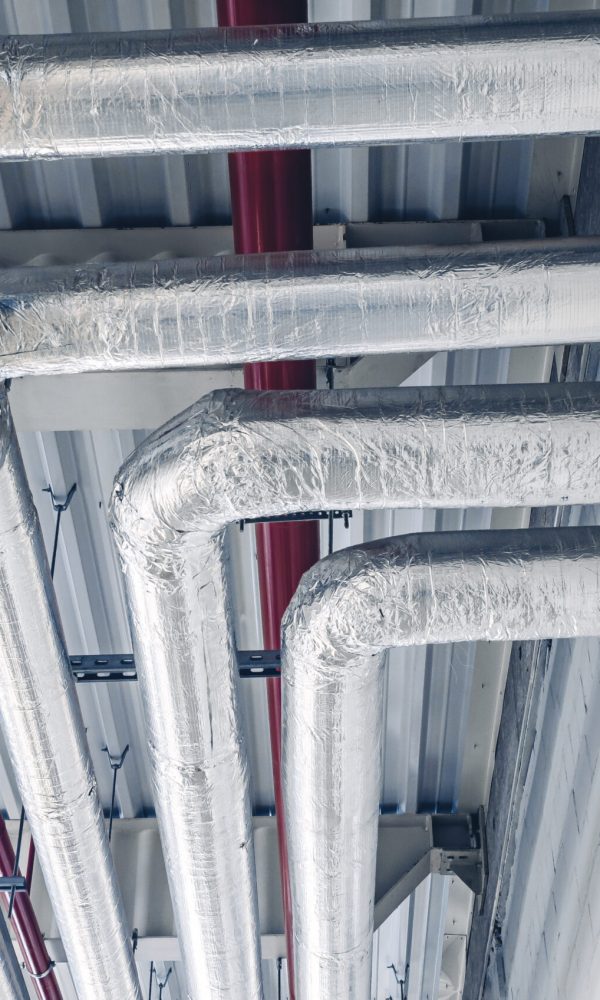 Metal pipes mounted under ceiling are covered with thermal insulation at modern production plant