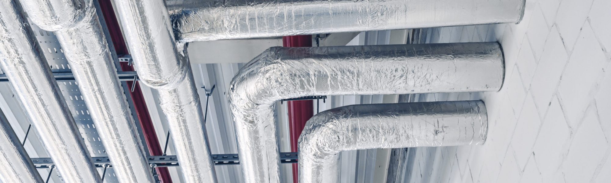 Metal pipes mounted under ceiling are covered with thermal insulation at modern production plant