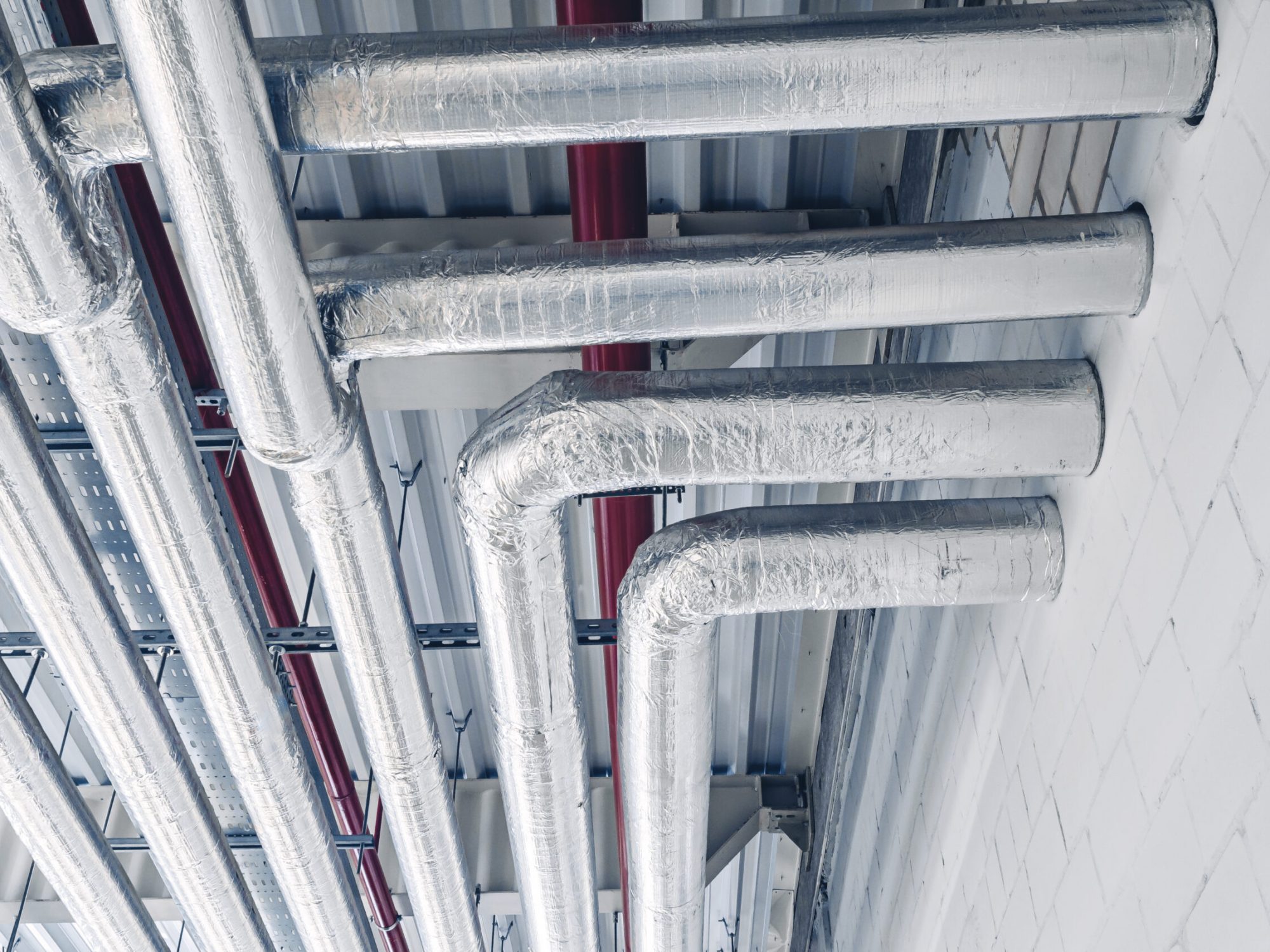 Metal pipes mounted under ceiling are covered with thermal insulation at modern production plant